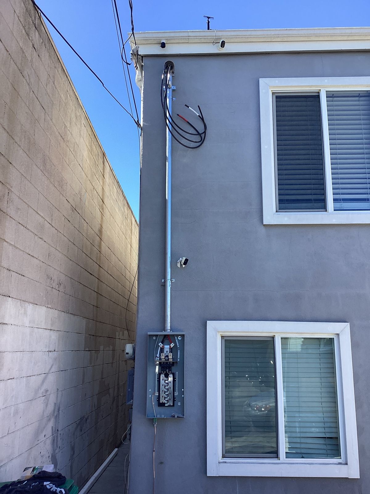 Electrical conduit and panel on gray building wall next to a narrow alley.