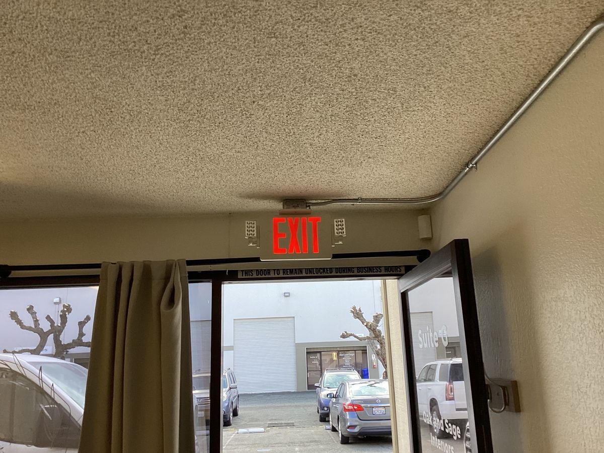 An EXIT sign above a doorway, with a view of cars and a building outside.