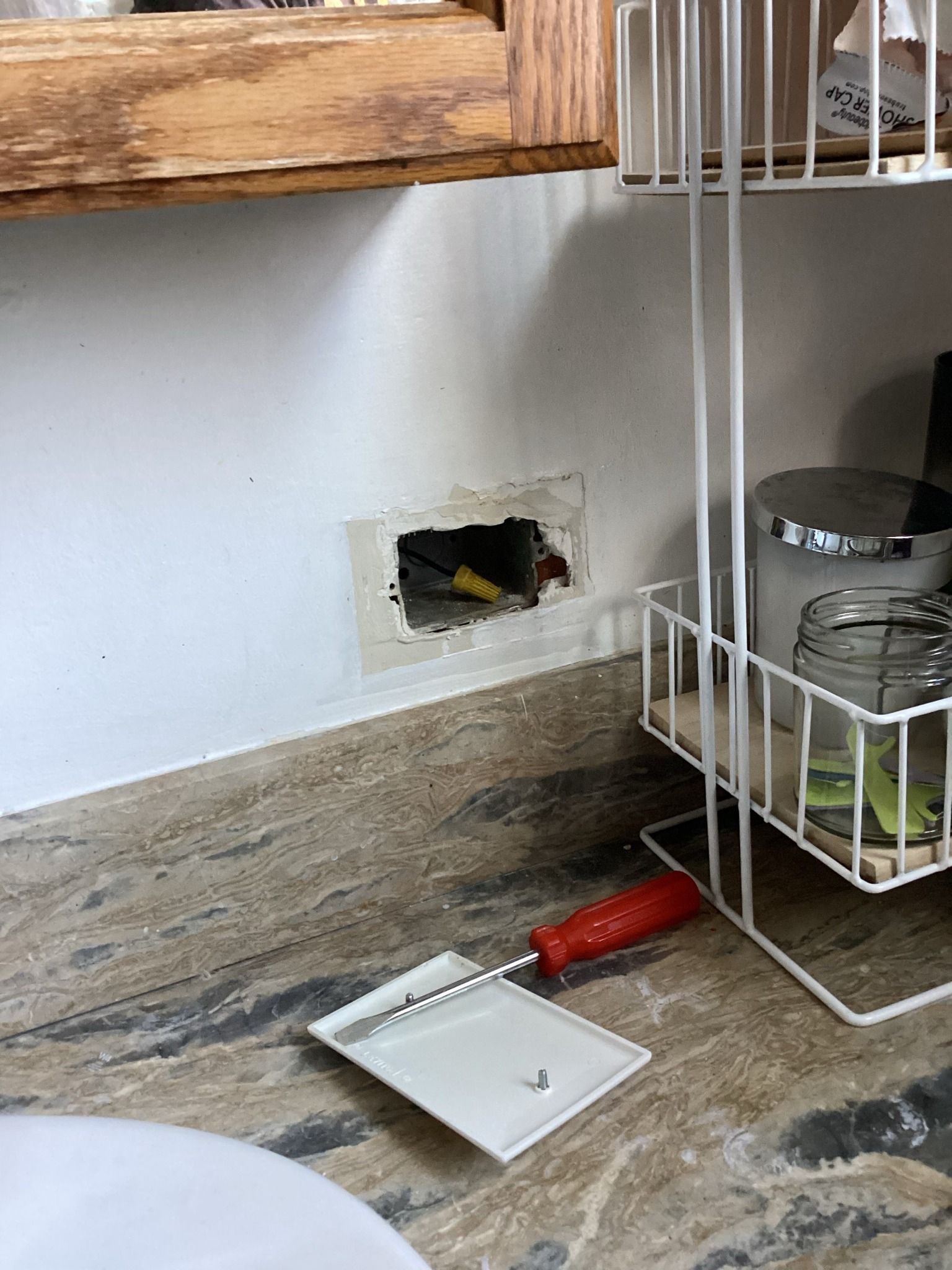 Exposed wall electrical wiring with hole. A putty knife and storage rack next to the damaged area.