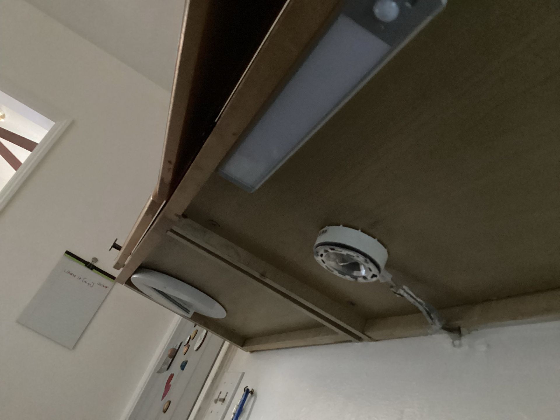 Underside of a wooden shelf with two circular lights and a rectangular light fixture attached.