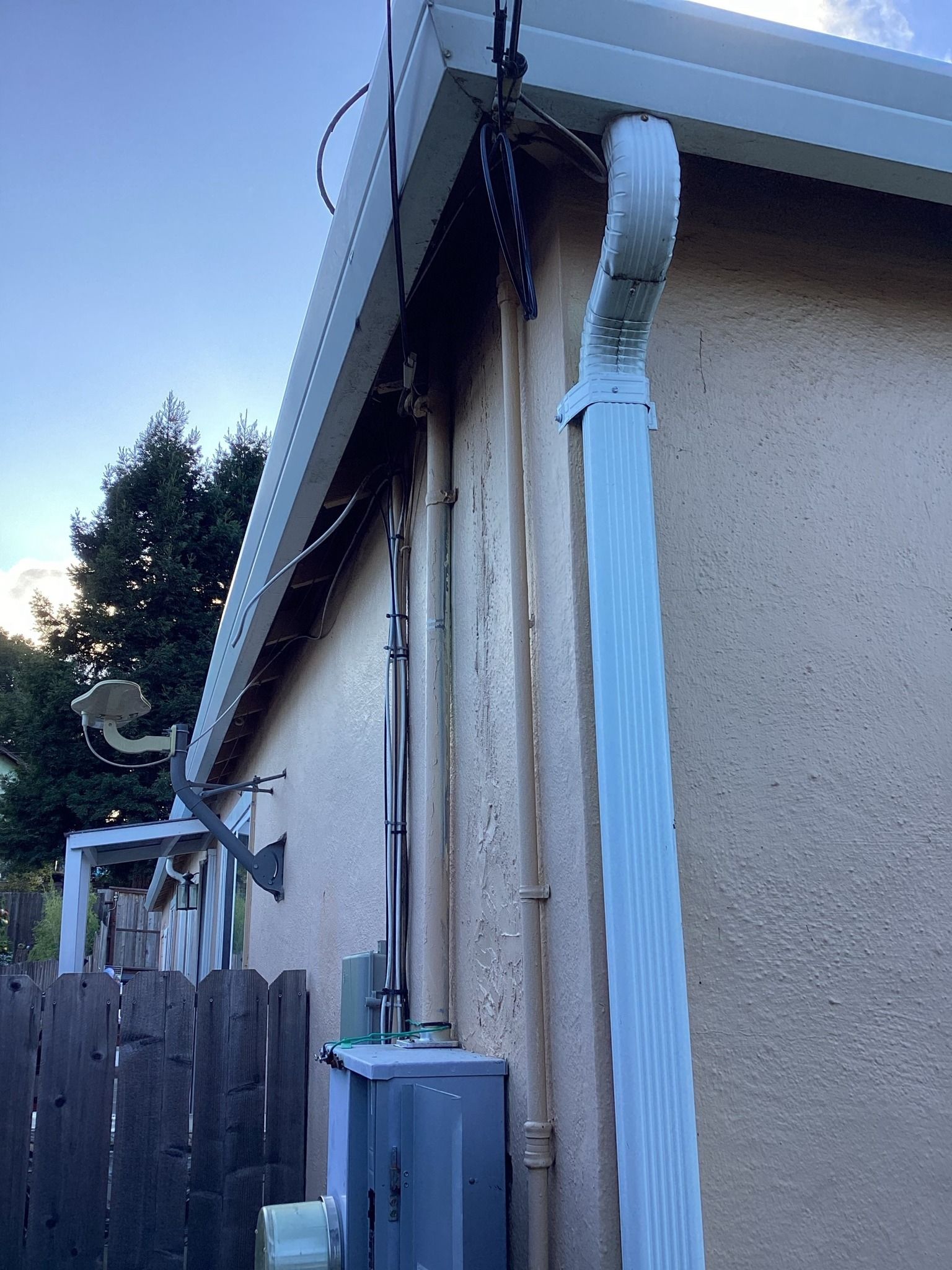 Exterior view of a beige stucco building with white gutters and various wires running along the side wall.