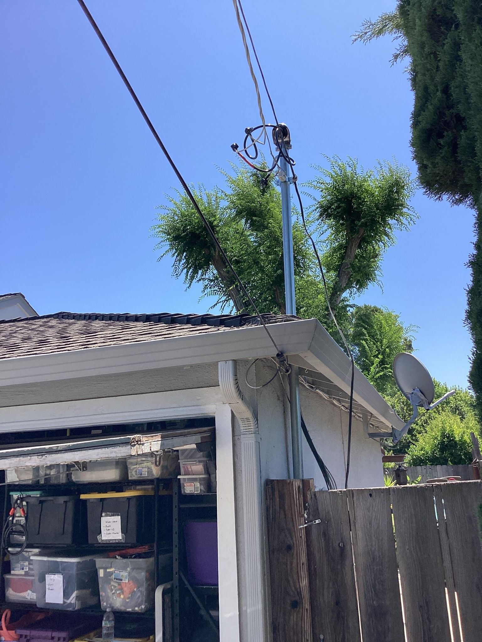Power lines atop a white garage with a partially visible fence and clear blue sky.