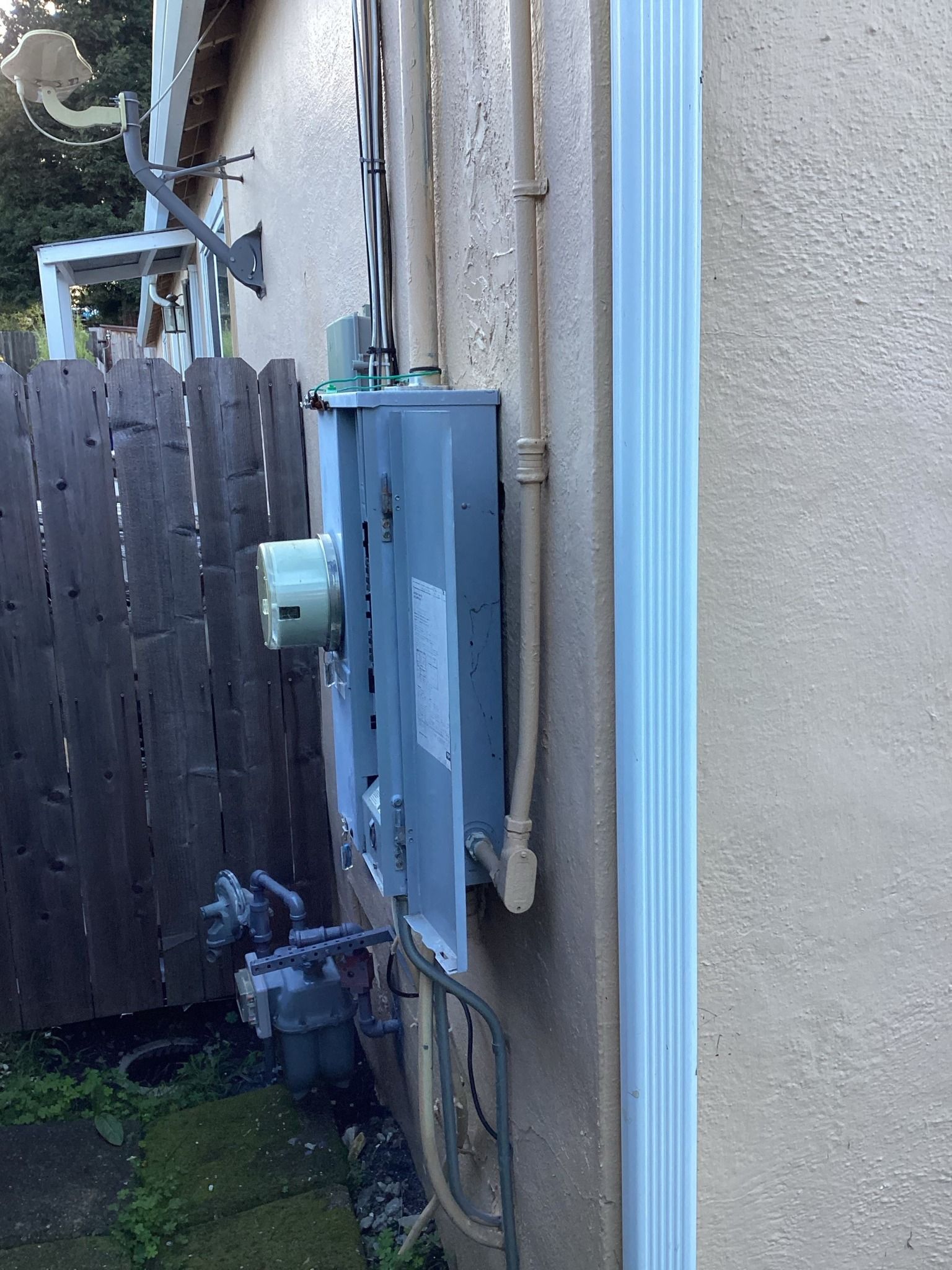Exterior electrical panel on a beige stucco wall next to a white rain gutter.