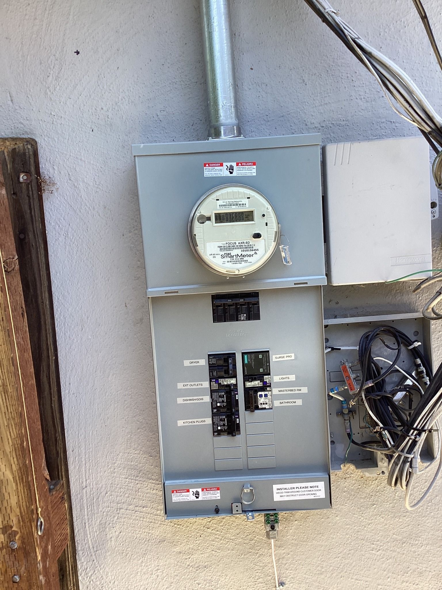 Electric meter and circuit breaker panel mounted on an exterior wall with conduit and wiring.