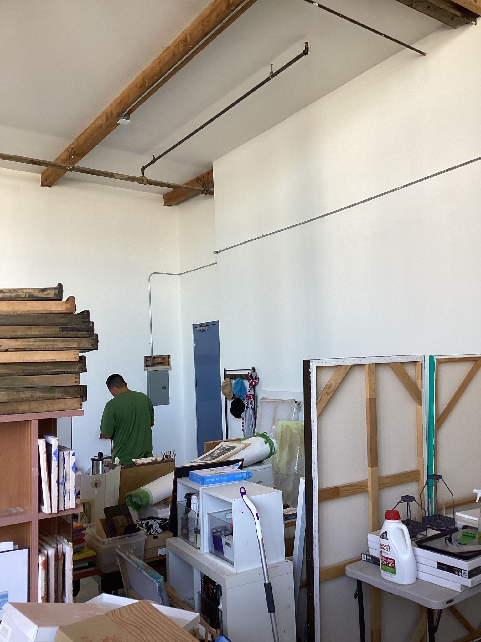 Art studio with an organized mess, an artist, and wooden beams overhead.