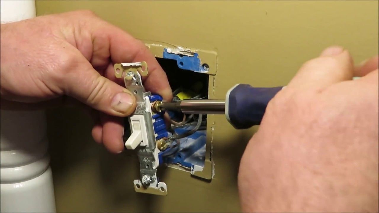 Person using a screwdriver to install a light switch in a wall.