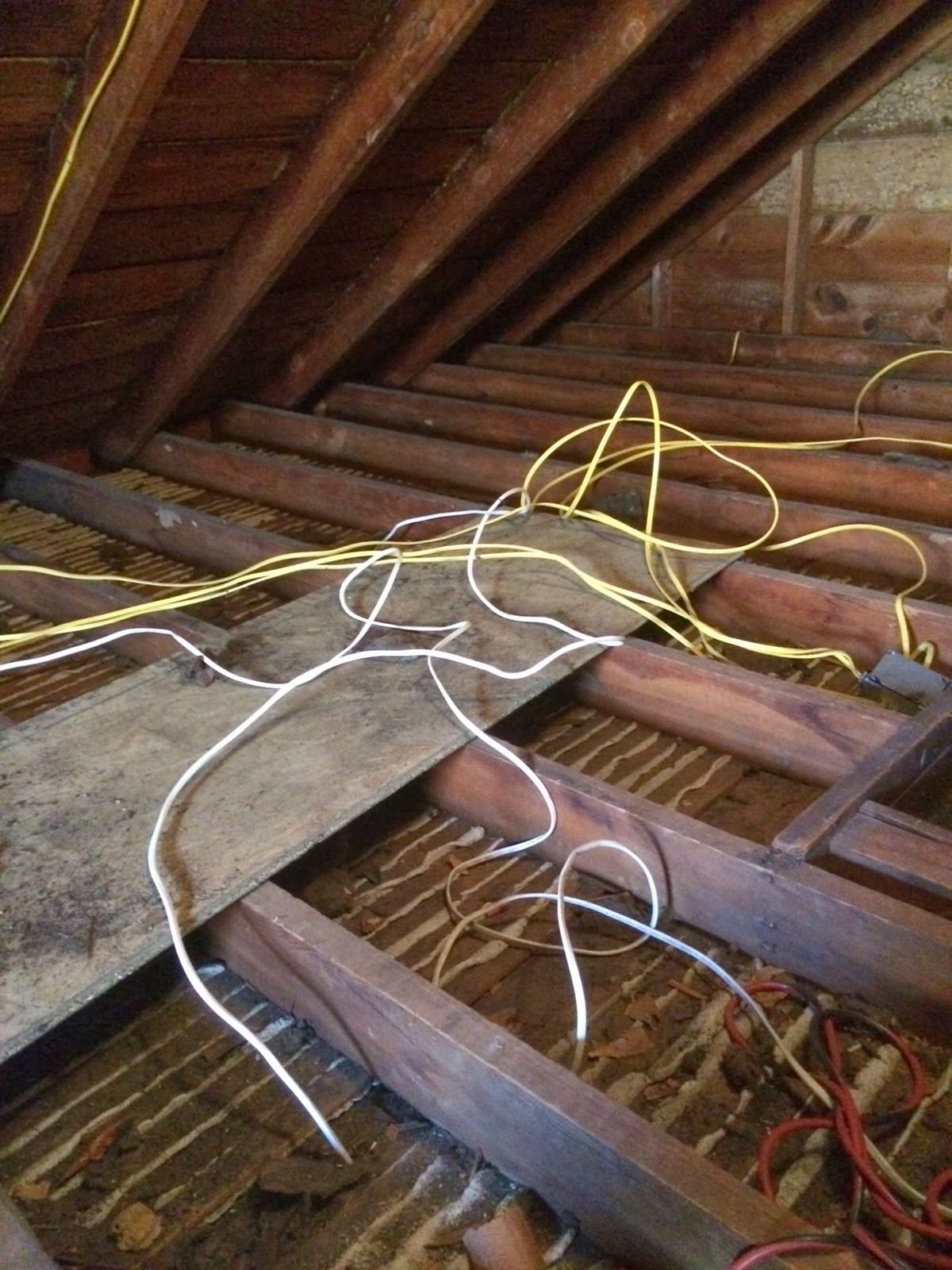 Yellow and white electrical wires tangled in an unfinished attic space, among wooden beams and boards.