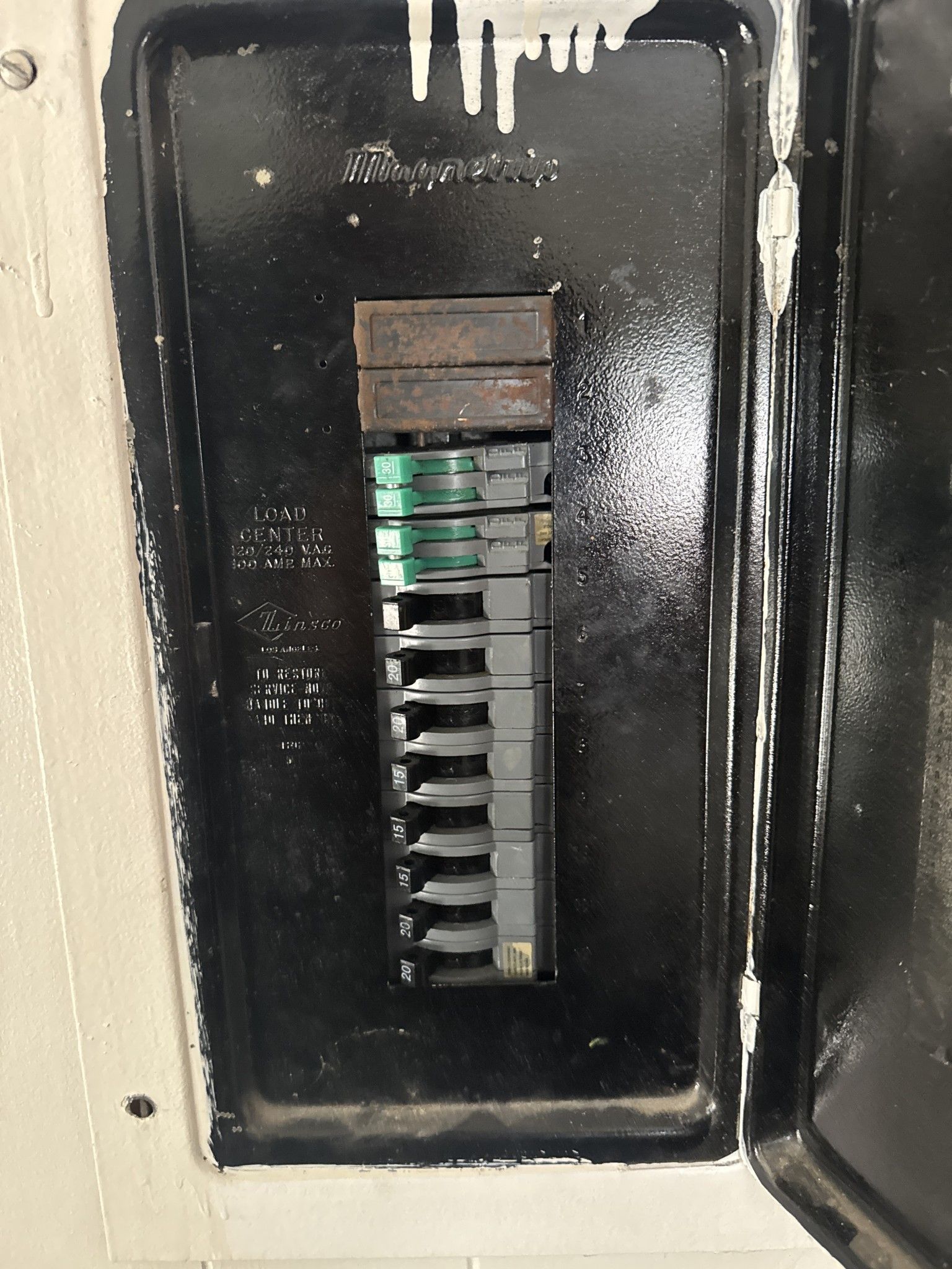 Black electrical panel with breakers in a white enclosure.