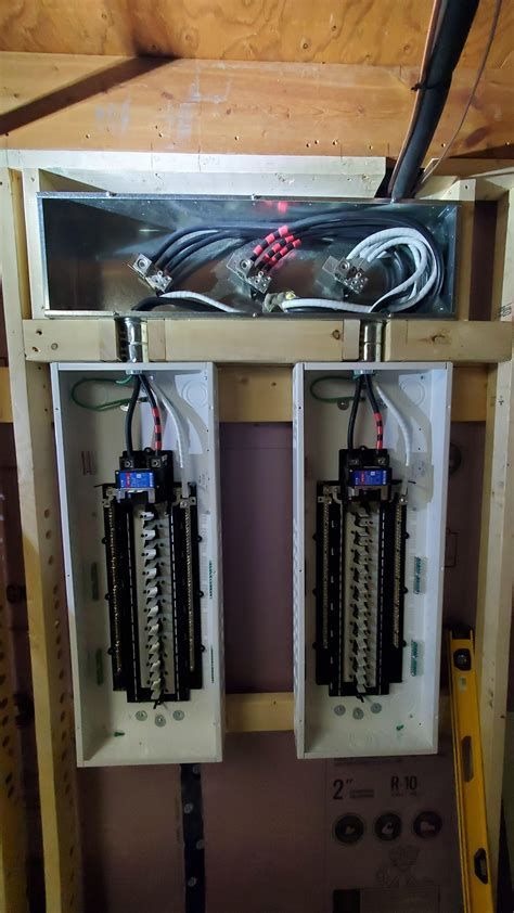 Two electrical breaker panels installed on a wooden frame, connected by wiring.