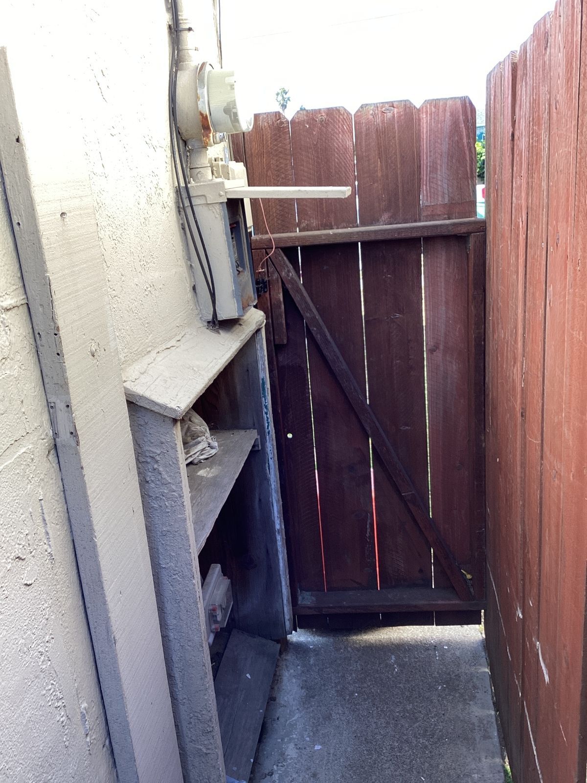 A narrow alleyway with a wooden gate and a utility box mounted on a stucco wall.
