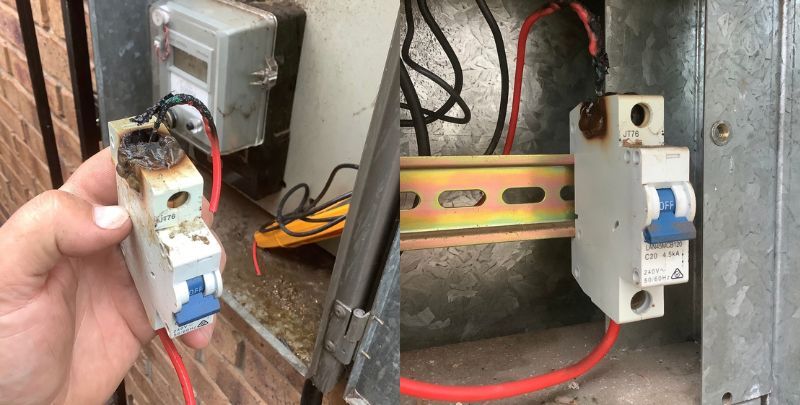 Burnt electrical circuit breaker held in hand, next to similar breaker in metal box, with exposed wires.