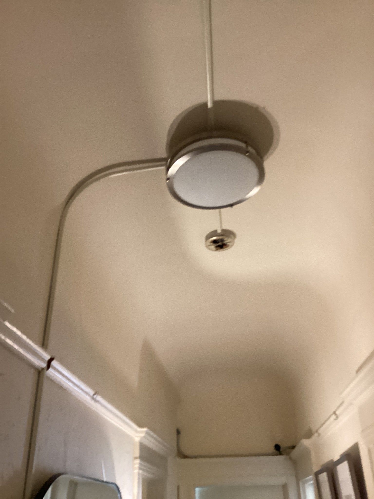 Ceiling light fixture with circular shade and silver conduit in a hallway.