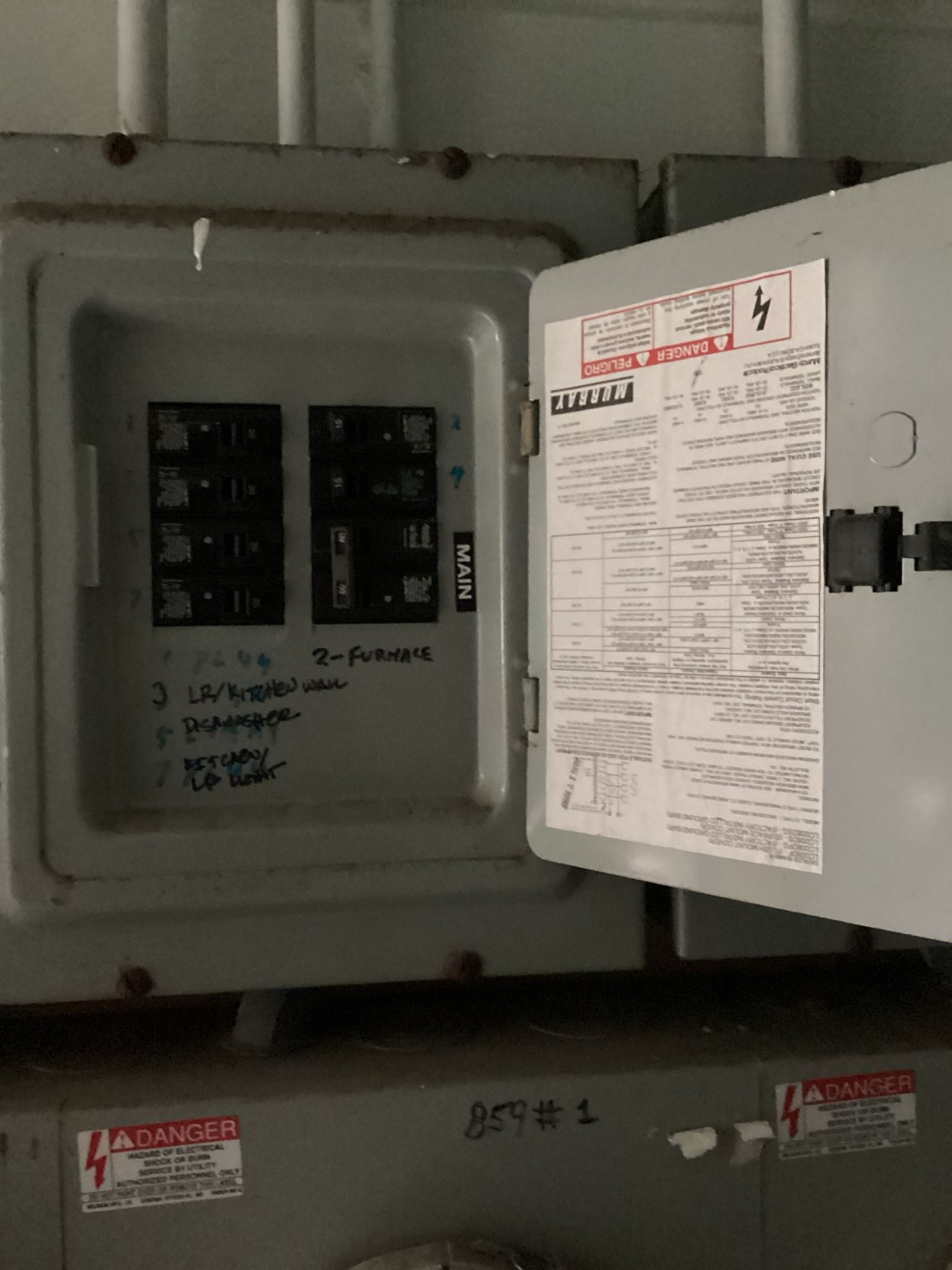 Open electrical panel with circuit breakers and documentation on the inside of the door.