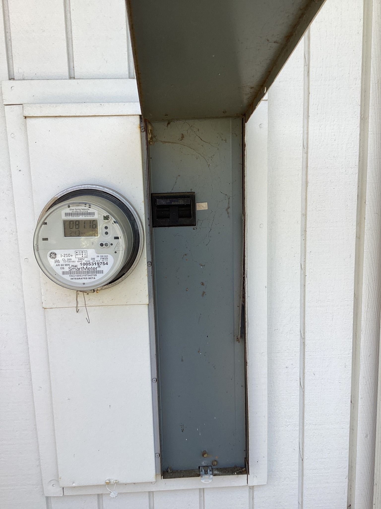 Electric meter and panel on a white house exterior with a partially open door.