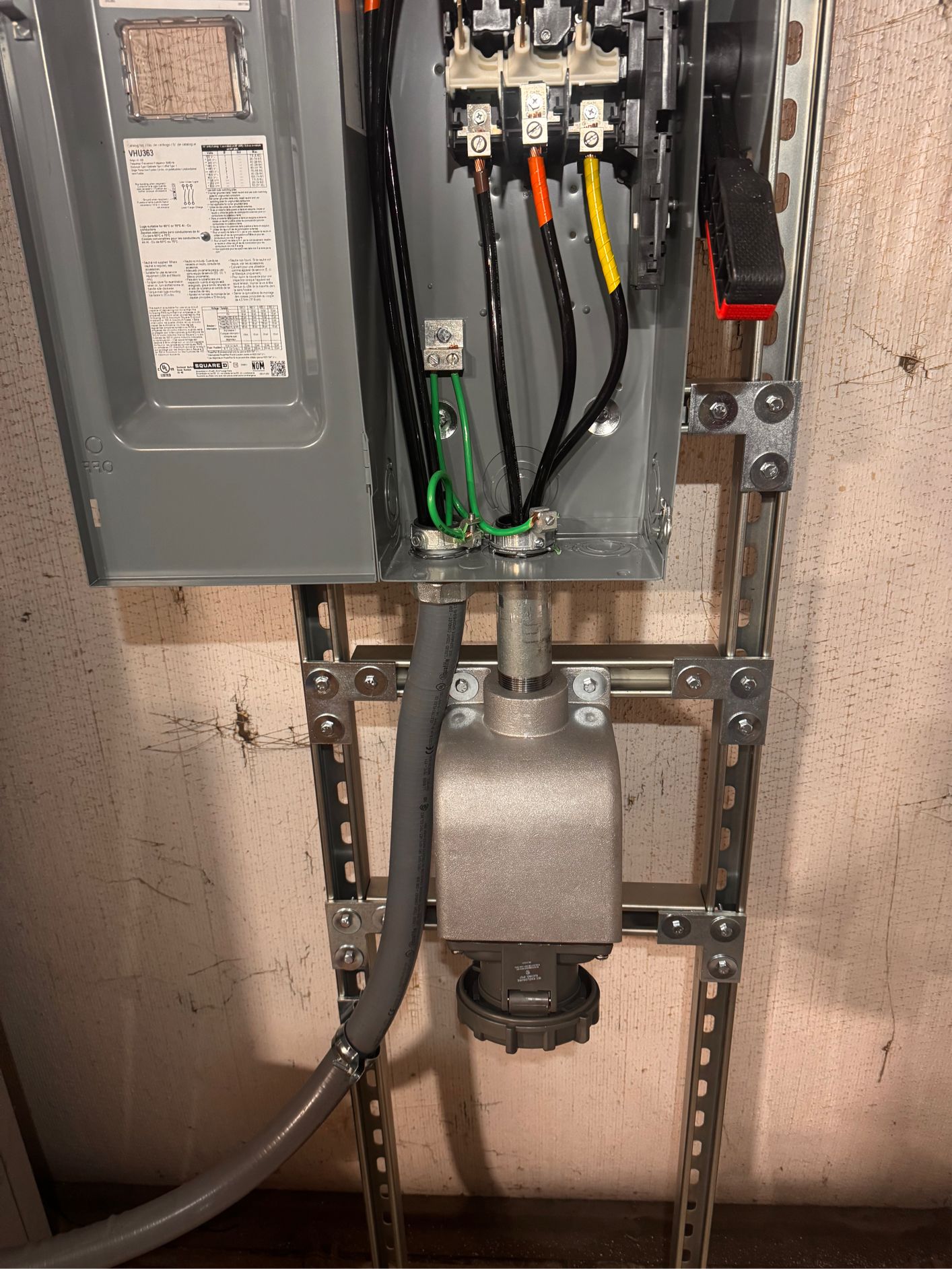 Electrical box with wires, conduit, and a plug, mounted on a metal frame, indoors.