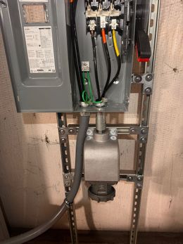 Electrical panel with wires connected, mounted on a metal bracket, with a plug at the bottom.