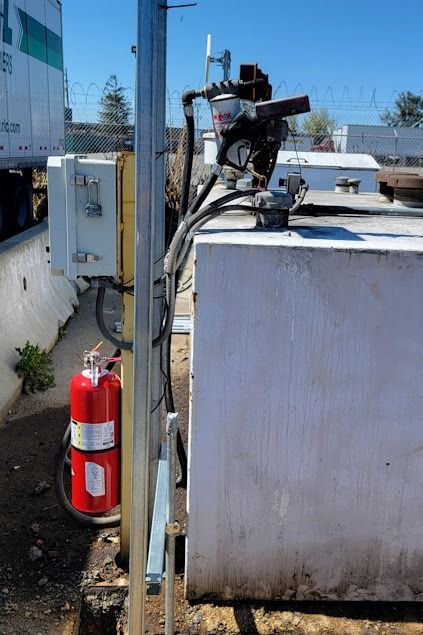Fire extinguisher near industrial equipment on white tank, outdoors.