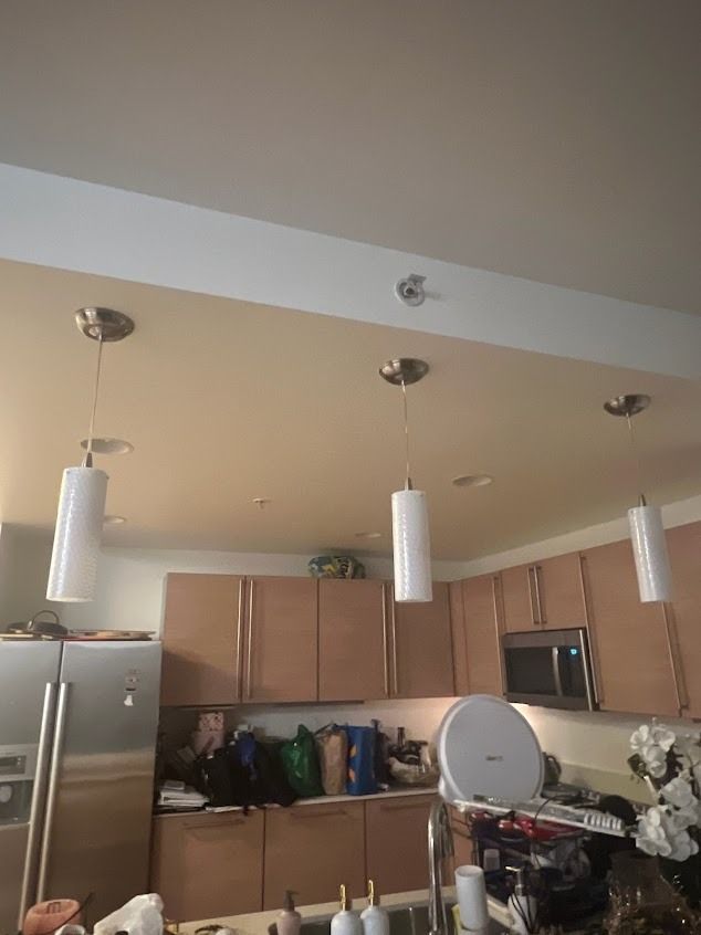 Kitchen with three pendant lights over cabinets, stainless steel refrigerator and microwave.