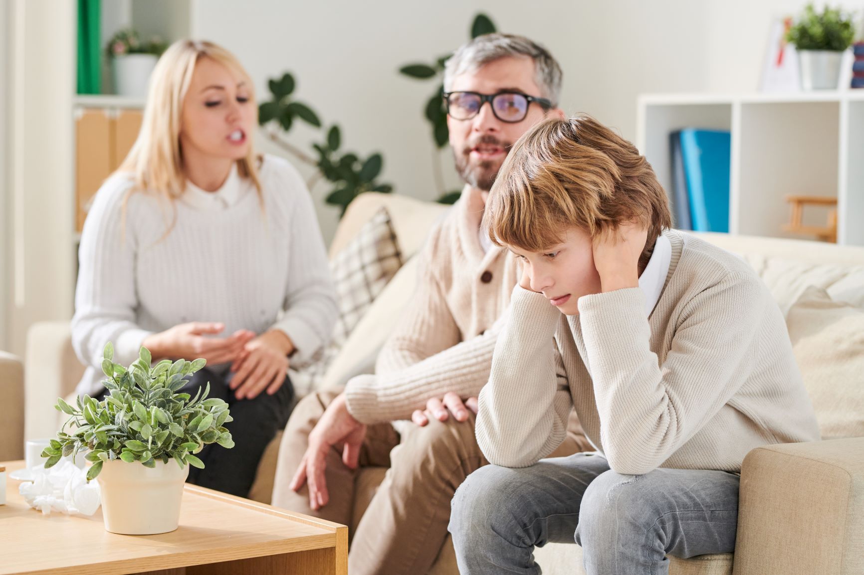 A young boy is sitting on a couch with his parents.