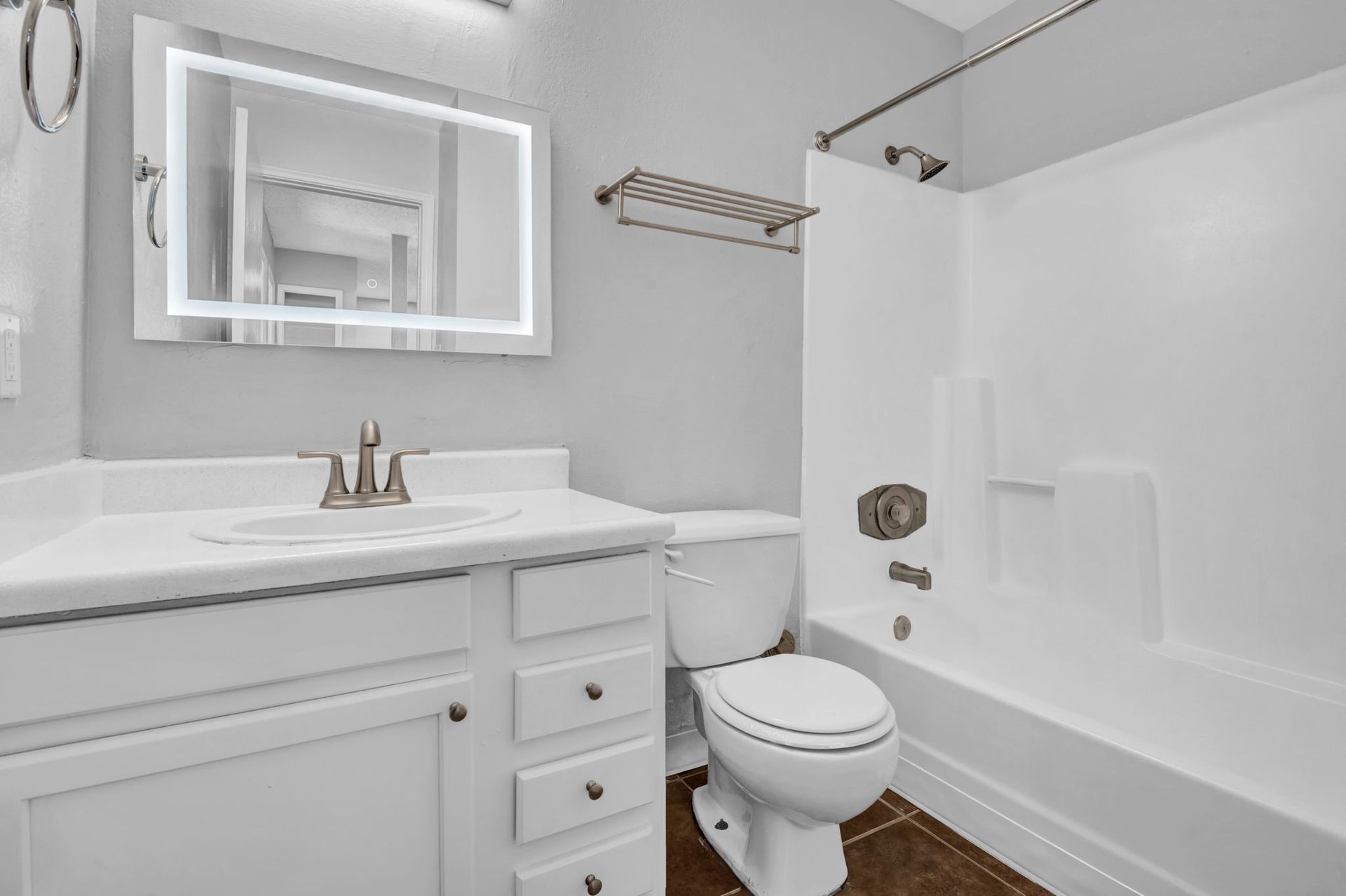 A renovated bathroom with white cabinetry, new hardware, a mirror with built in modern designer lighting, and quartz countertops.
