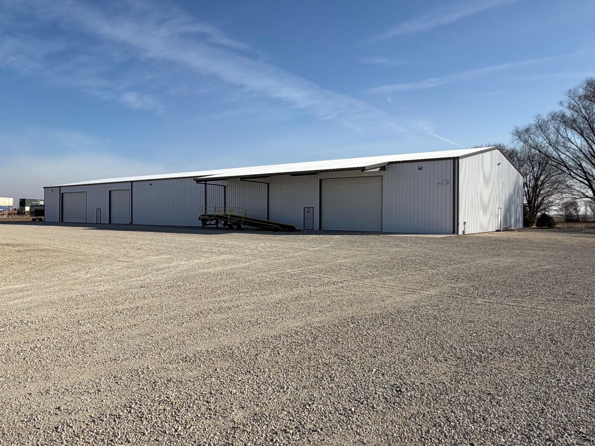 White warehouse building on gravel under a blue sky with sparse clouds.