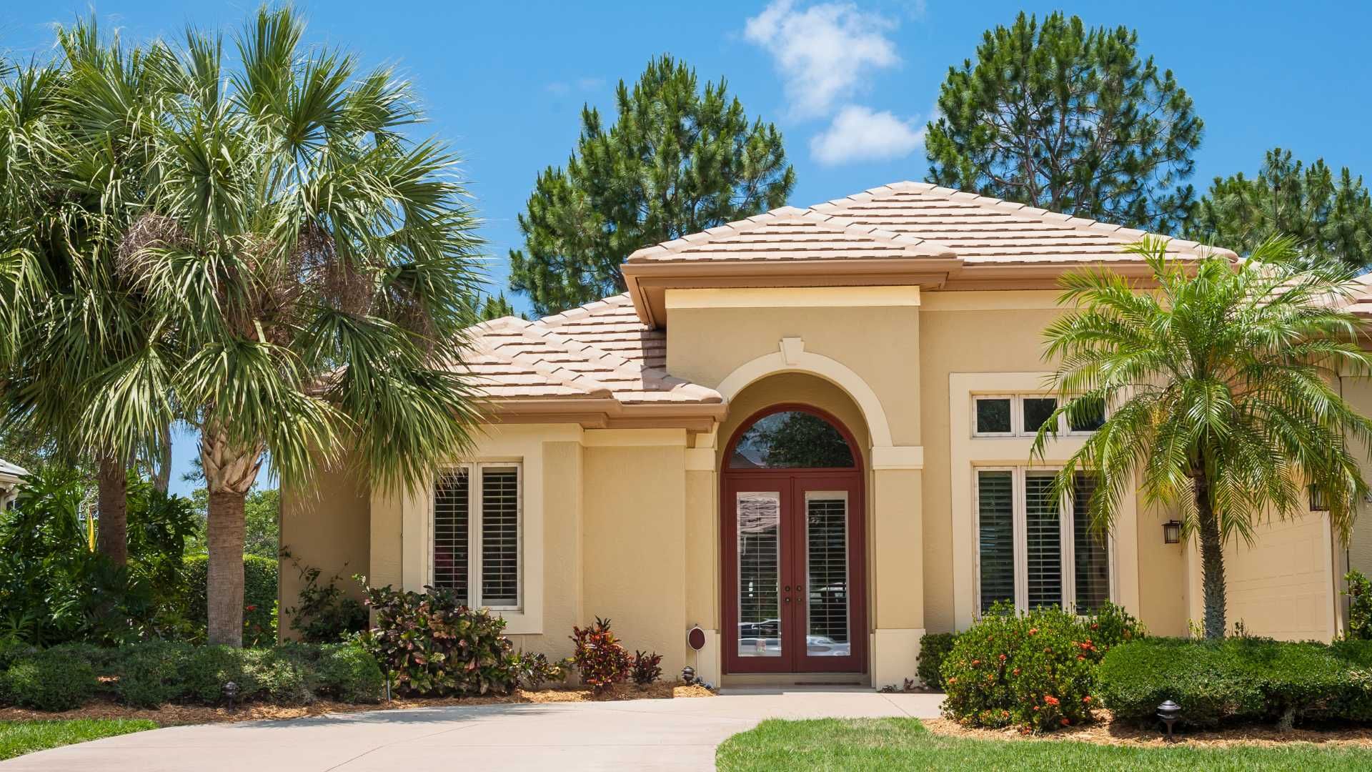 Beige stucco house with a tiled roof and a red door. Palm trees in the front yard.