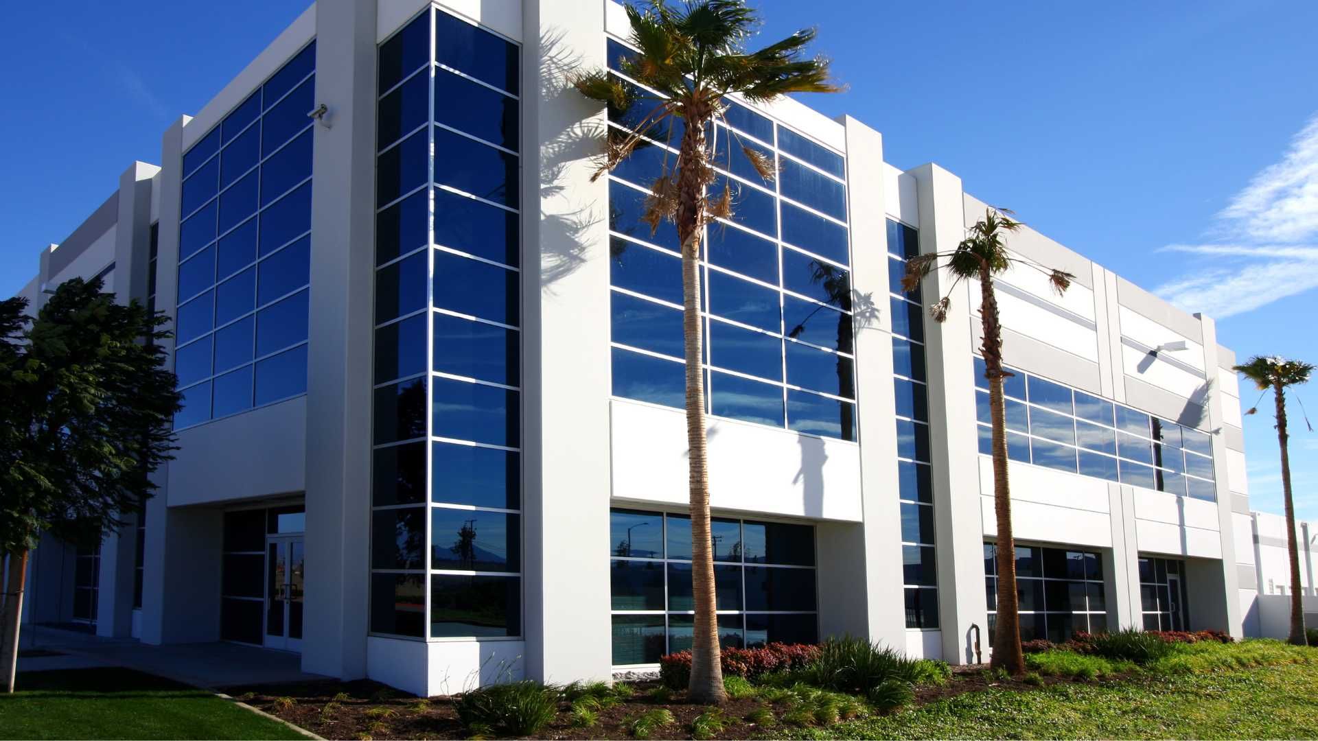 Modern, white, multi-story office building with large blue-tinted windows. Palm trees are in front of the building.