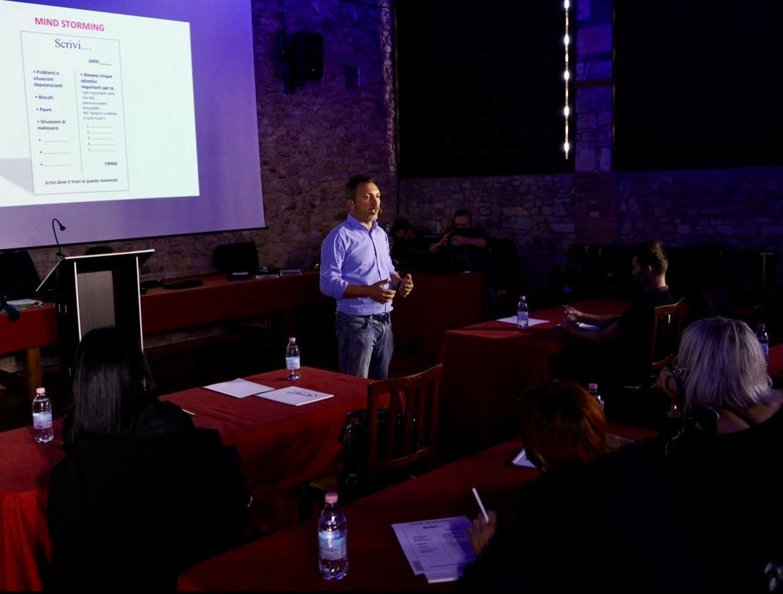 Un hombre realiza una presentación en una conferencia con una pantalla de proyector en una sala con poca luz.