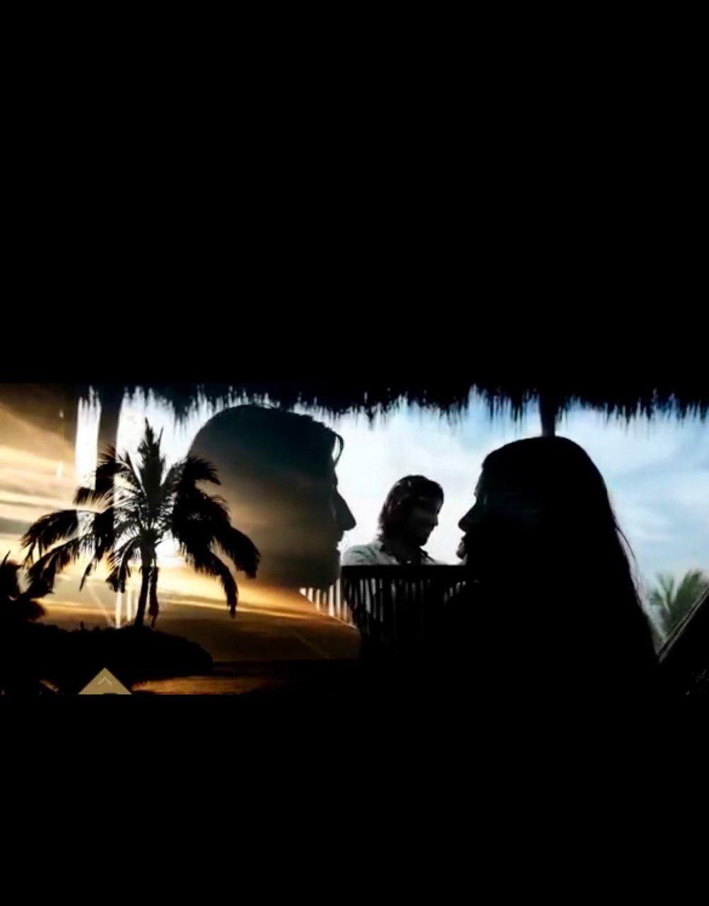 Coppia in silhouette sotto un tetto di paglia, palme al tramonto.