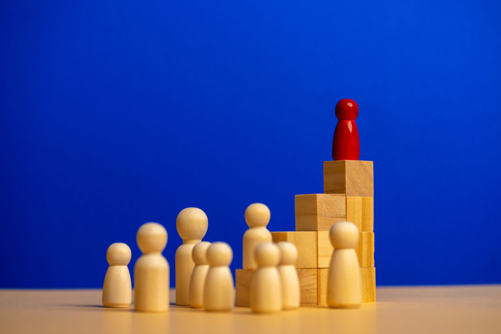 Figuras de madera: una roja sobre un escalón de bloques, otras de pie debajo. Fondo azul.