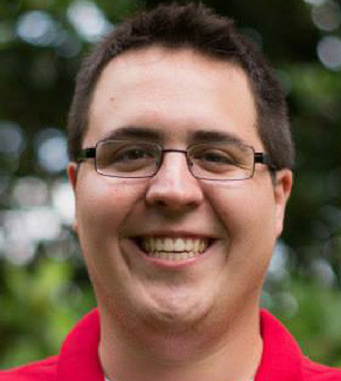 A man wearing glasses and a red shirt is smiling for the camera.