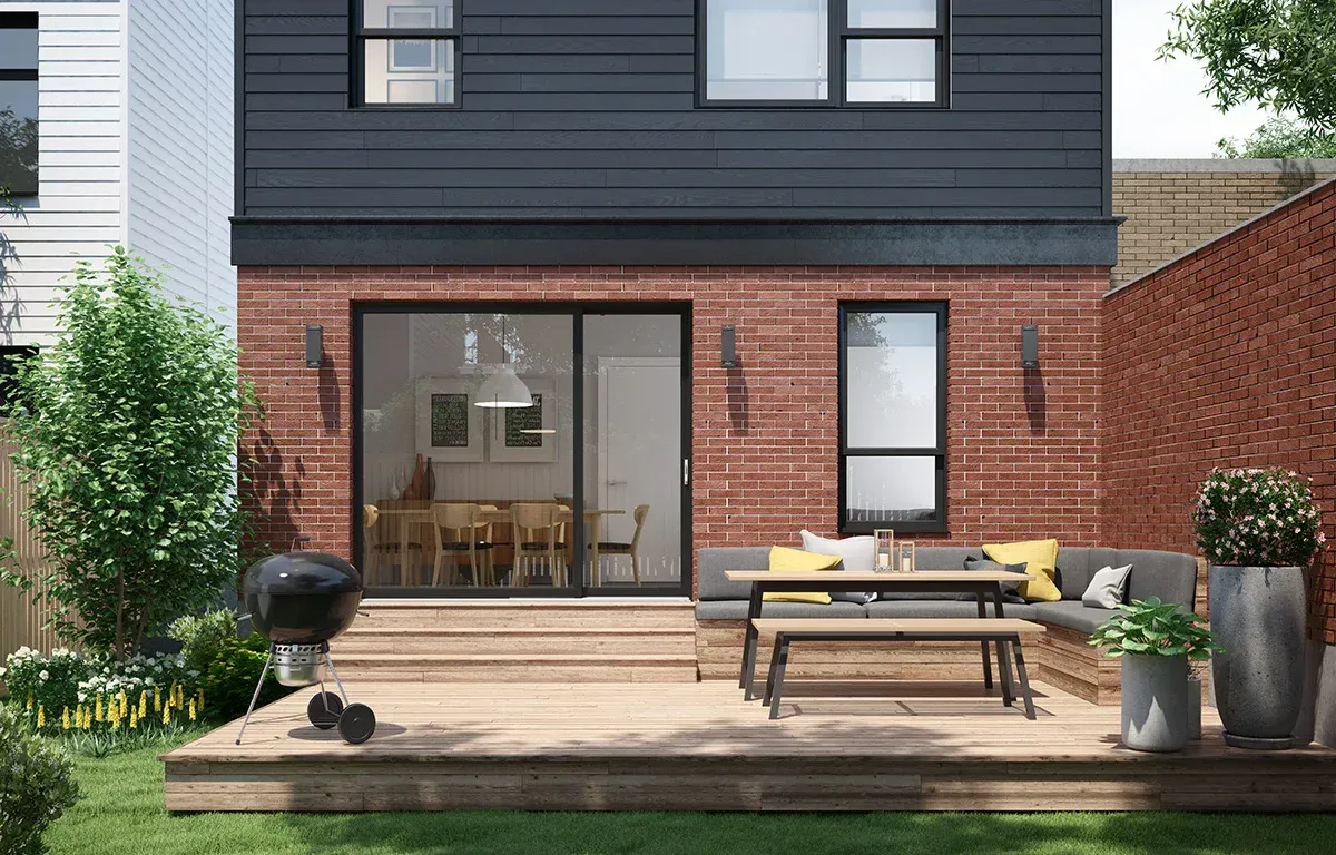 Backyard patio with wooden deck, brick walls, and outdoor seating; a grill sits to the side with the house in the background.