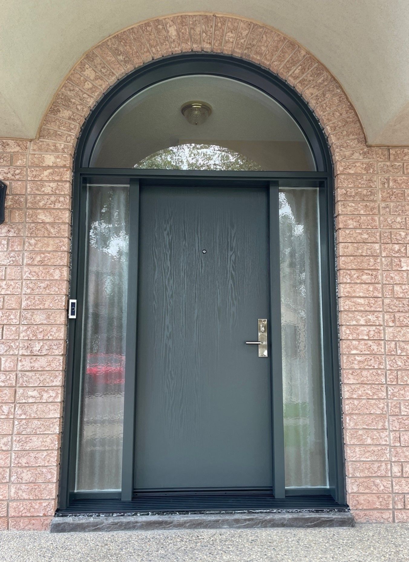The front door of a brick house with a black door and arched window.