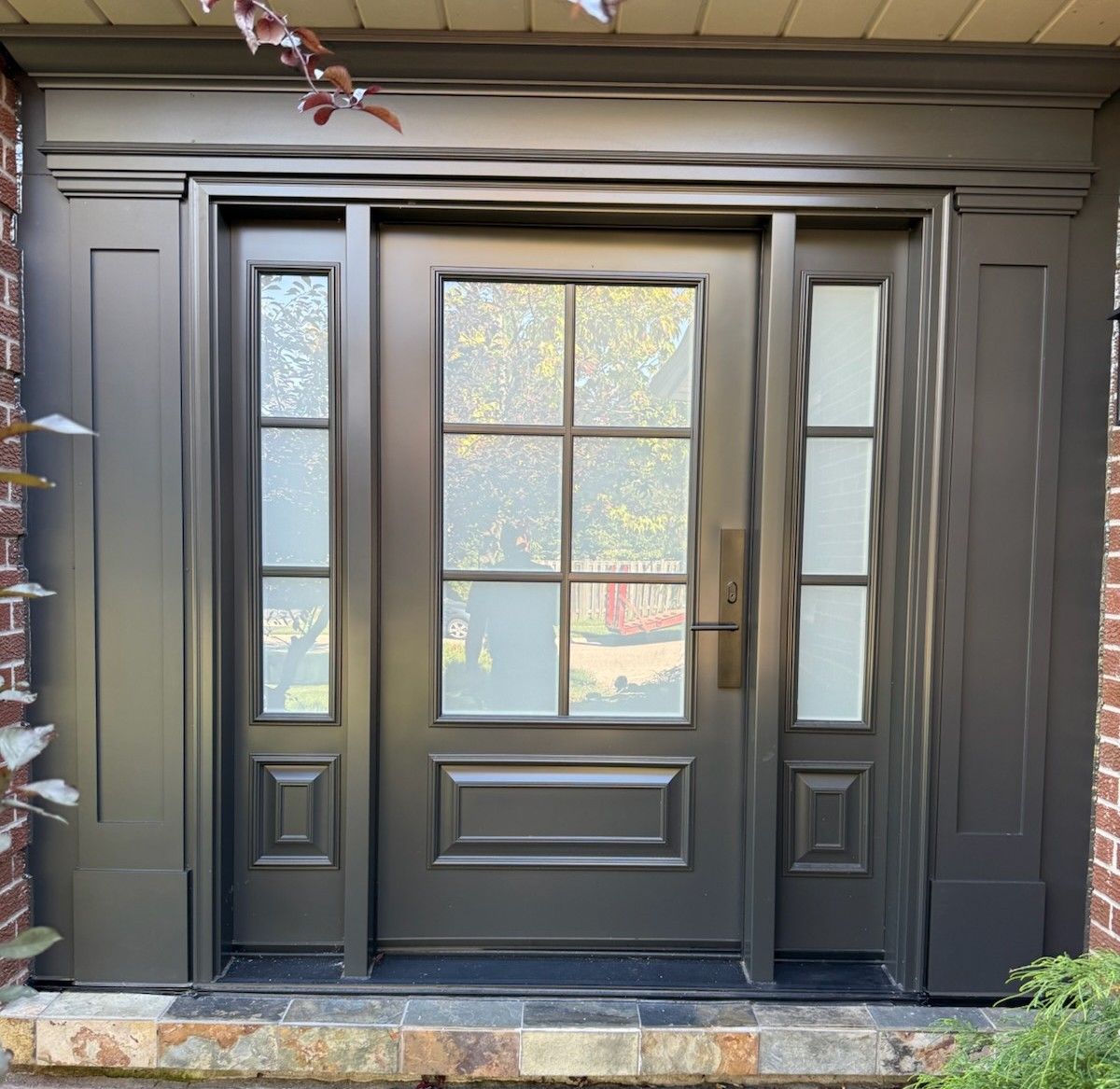 Dark gray front door with sidelights, brick surround, and stone steps.