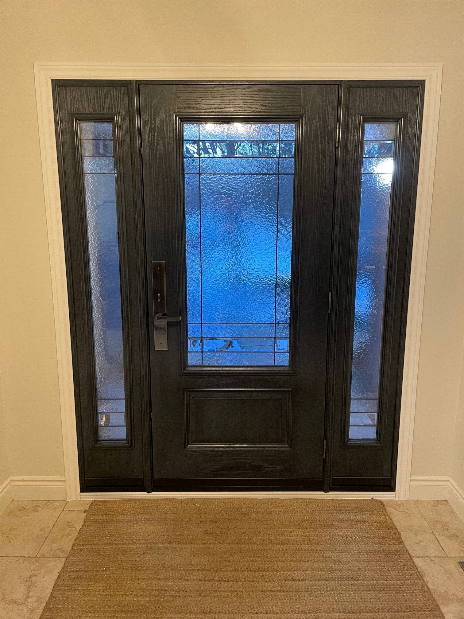 A black door with a stained glass window and a rug in front of it.