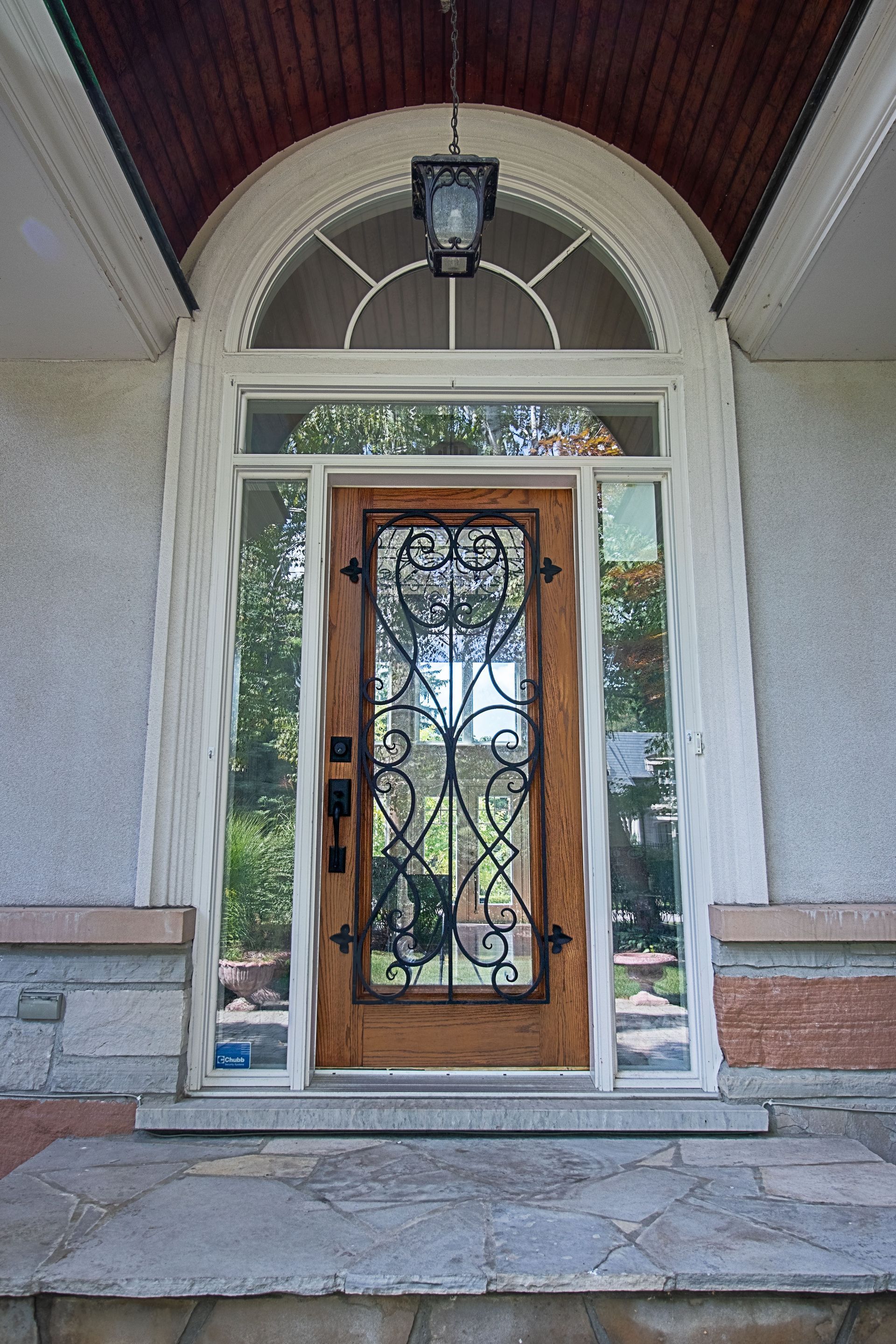 The front door of a house with a wrought iron door and a lantern hanging from the ceiling.