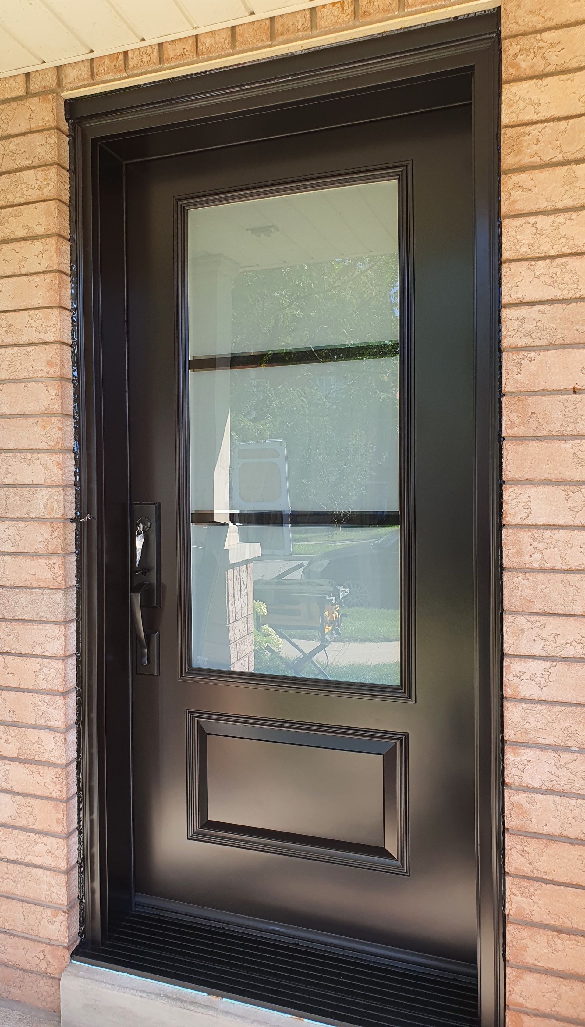 A black door with a glass window is on a brick wall.