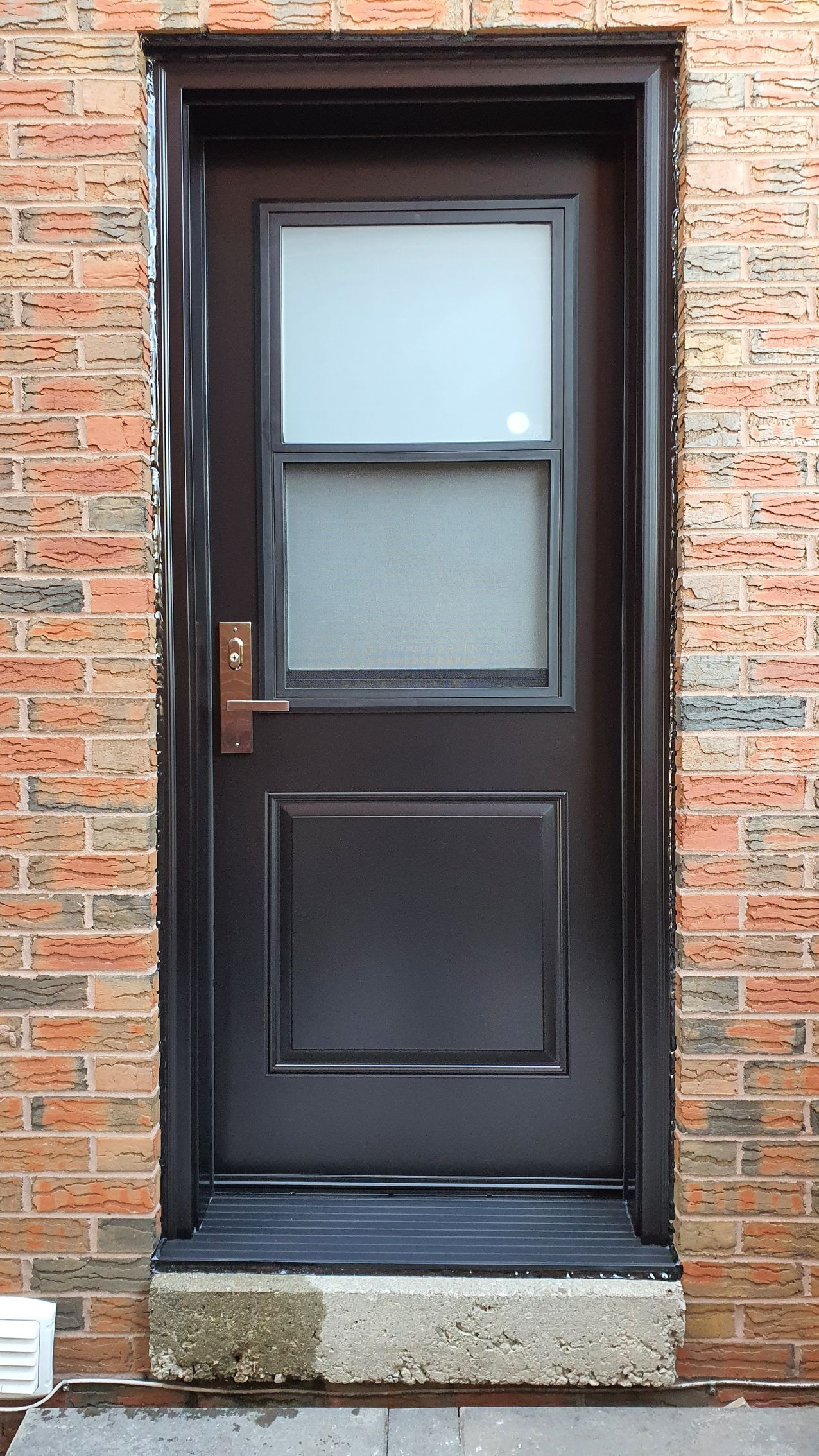 A brown door with a glass window is on a brick wall.