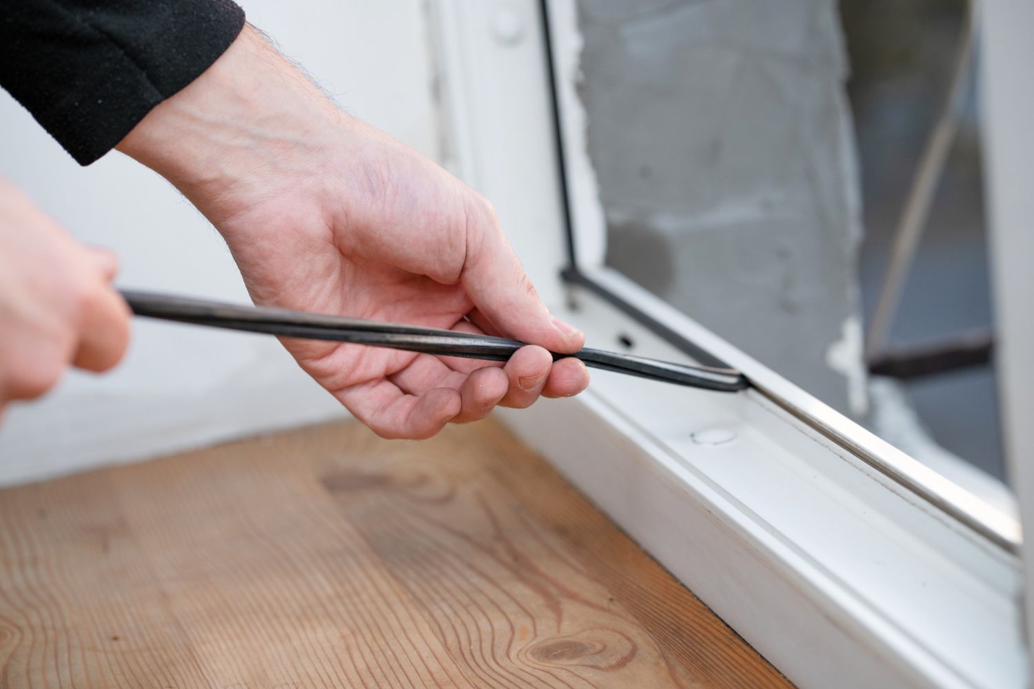 Person using a tool to remove a black seal from a white window frame, close up.