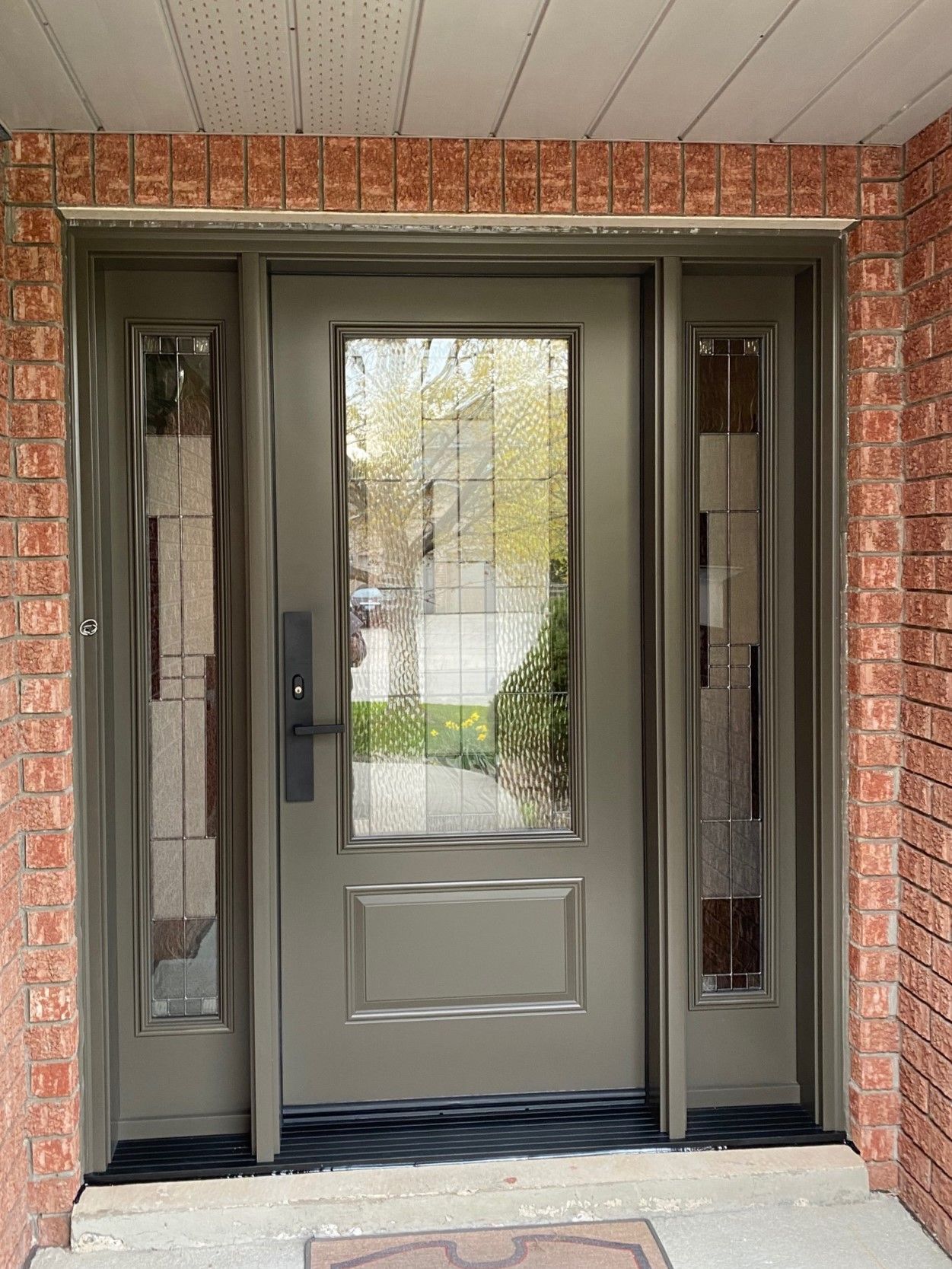 The front door of a house with a brick wall and a gray door.