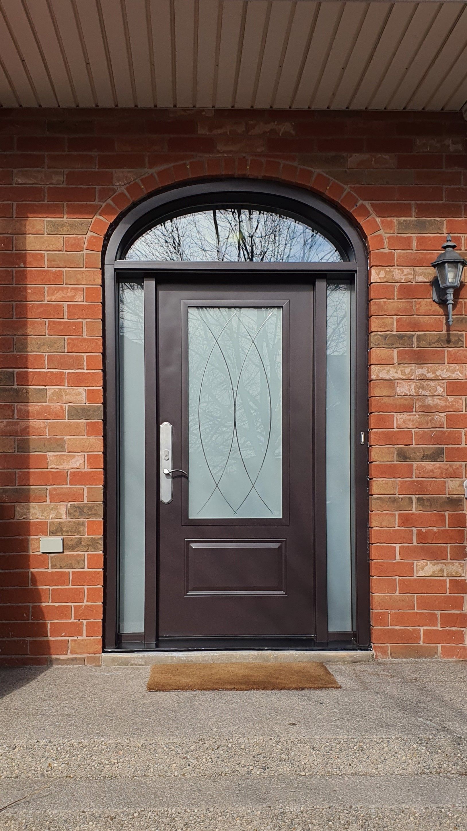 The front door of a brick house with a brown door and a stained glass window.
