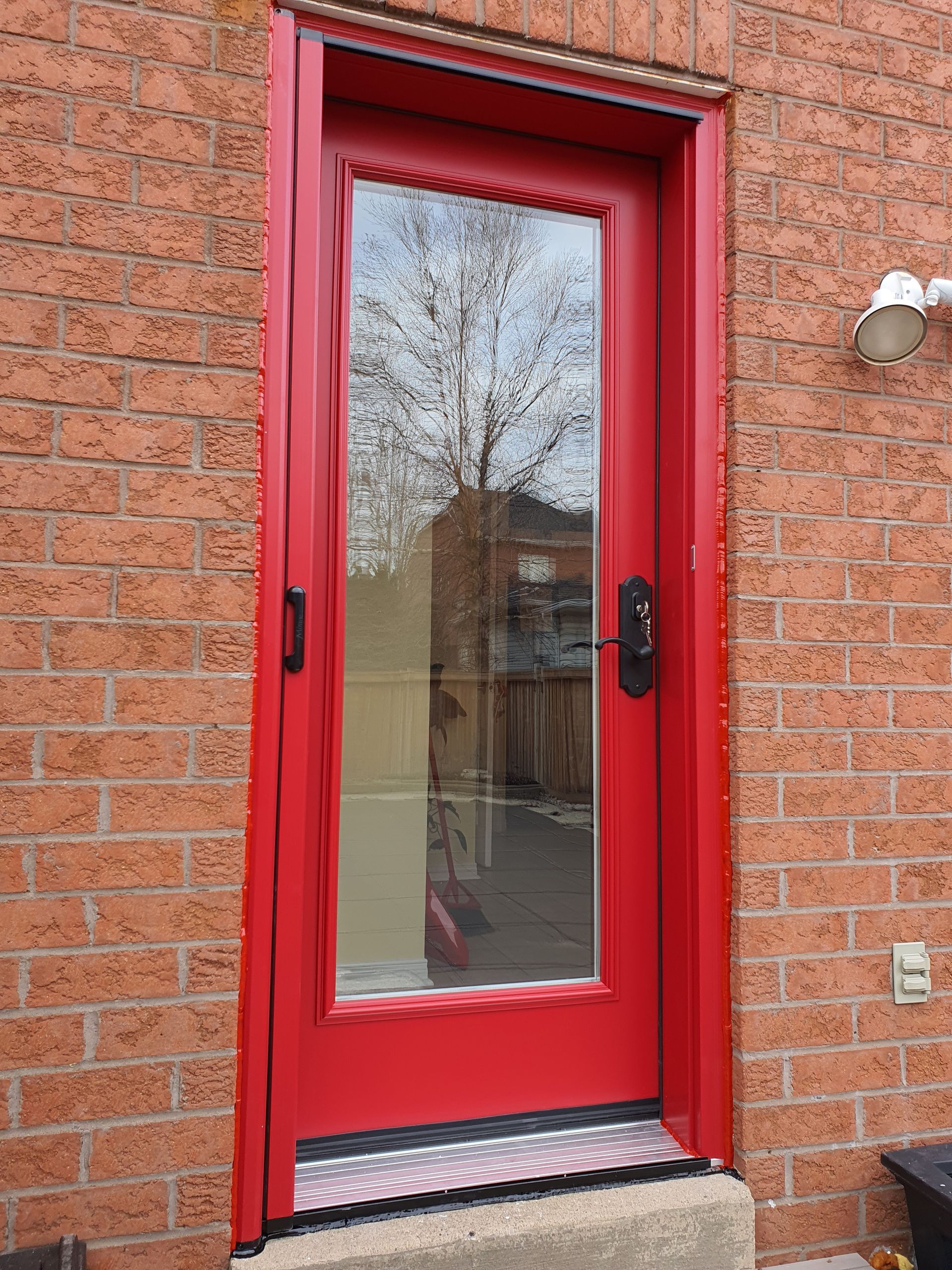 A red door with a glass window is on a brick wall.