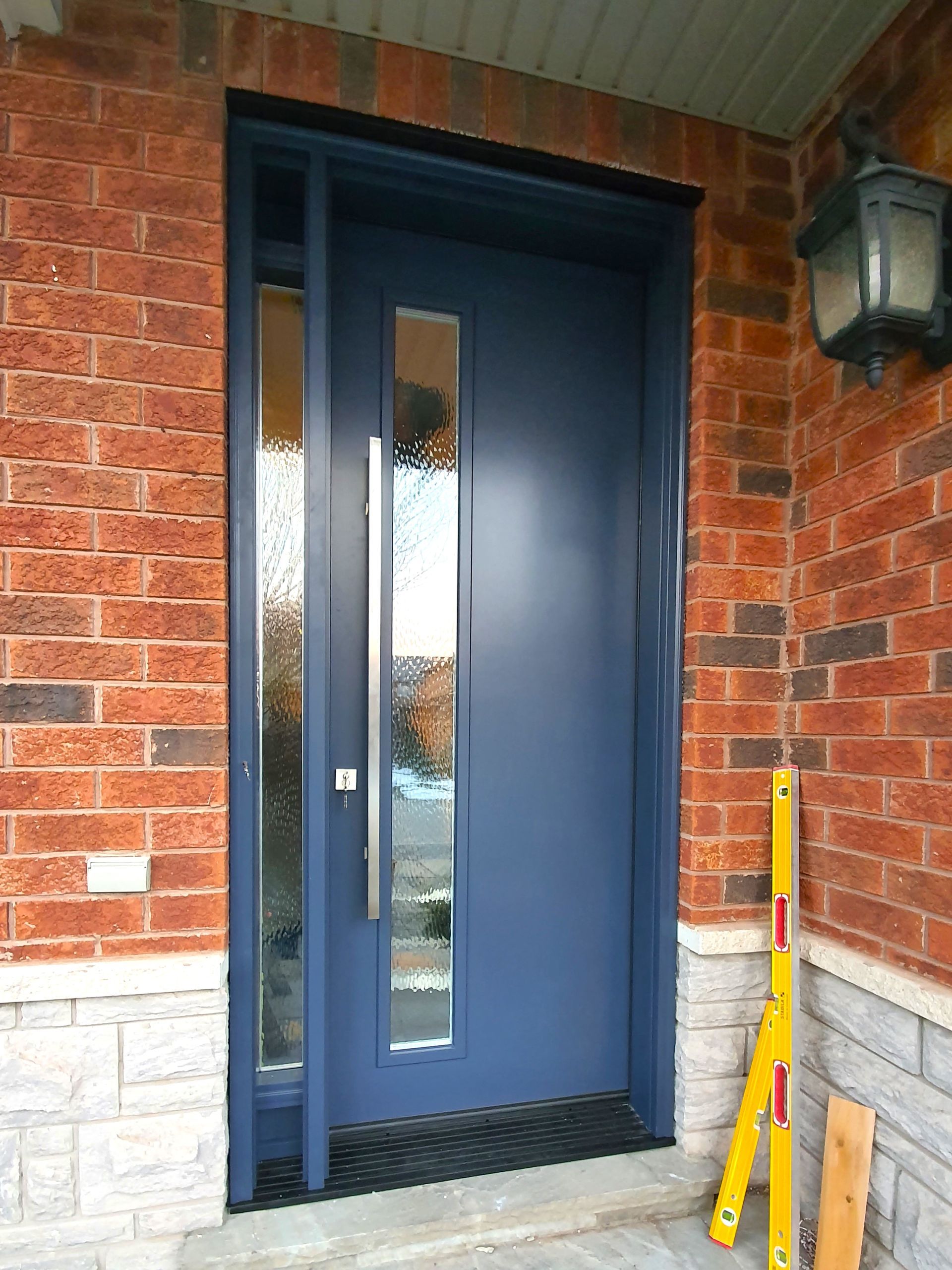 A blue door is on a brick wall next to a yellow level.