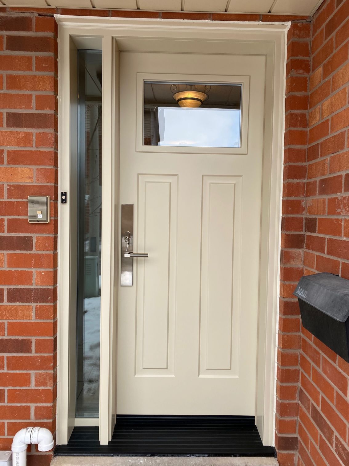 A white door with a small window is on a brick wall.