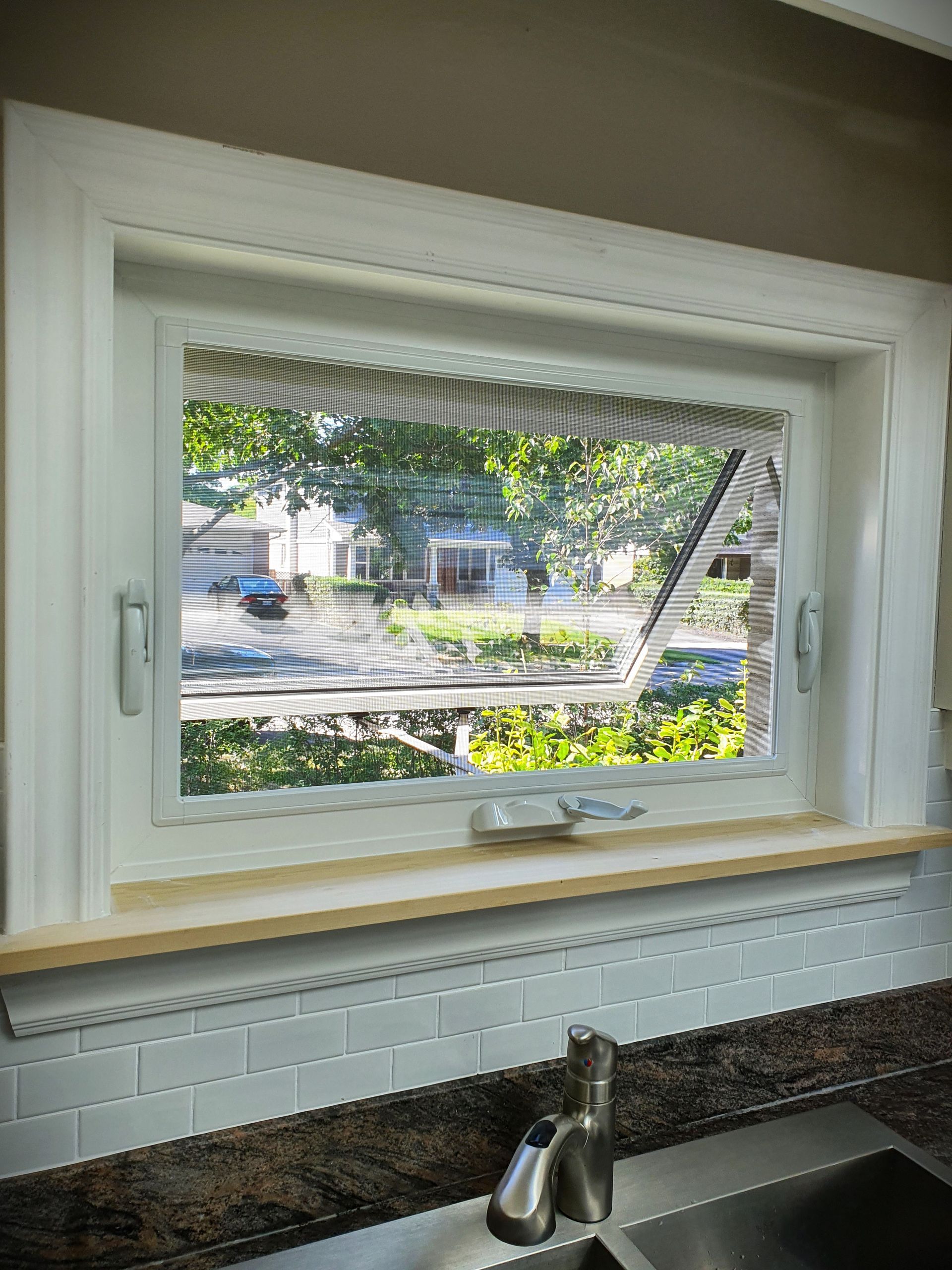 A kitchen with a sink and a window with a view of a house.