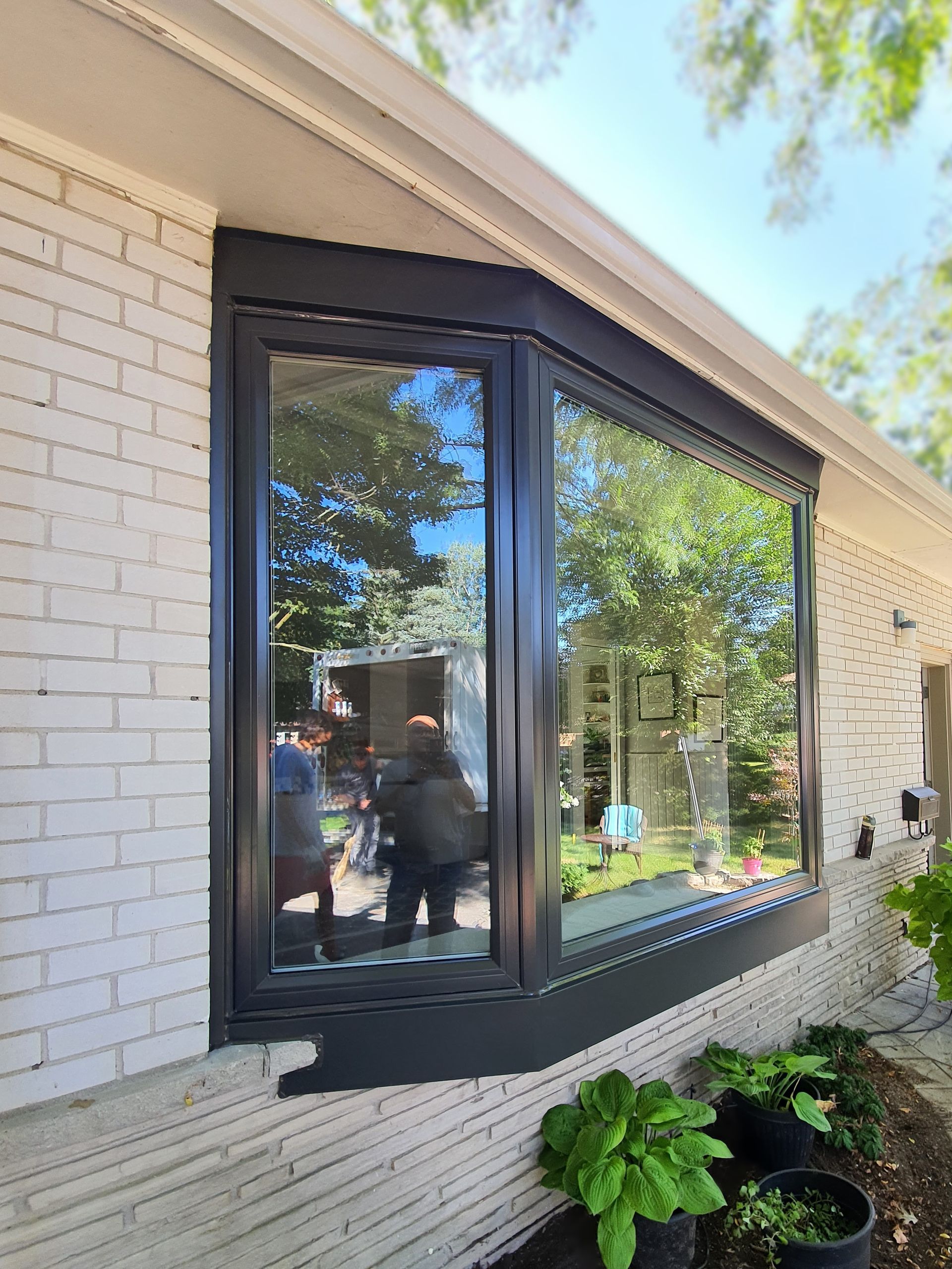 A large bay window on the side of a white brick house.