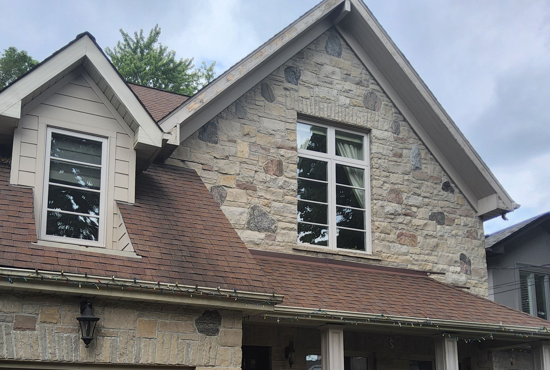 Stone-walled house with a brown roof and white-framed windows against a cloudy sky.