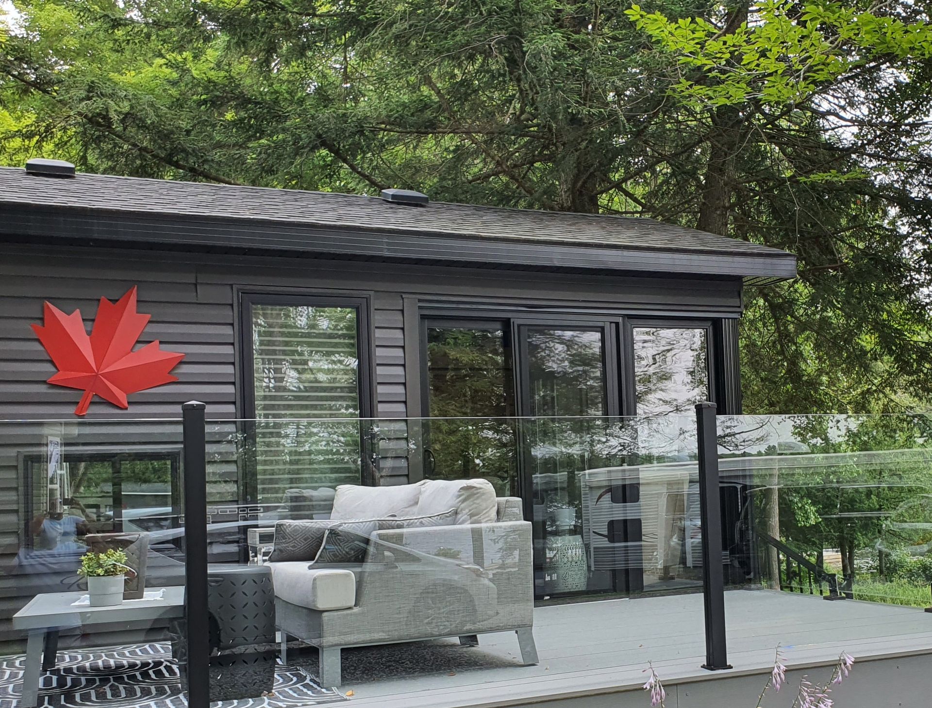 Deck with gray furniture, glass railing, red maple leaf, and cabin.