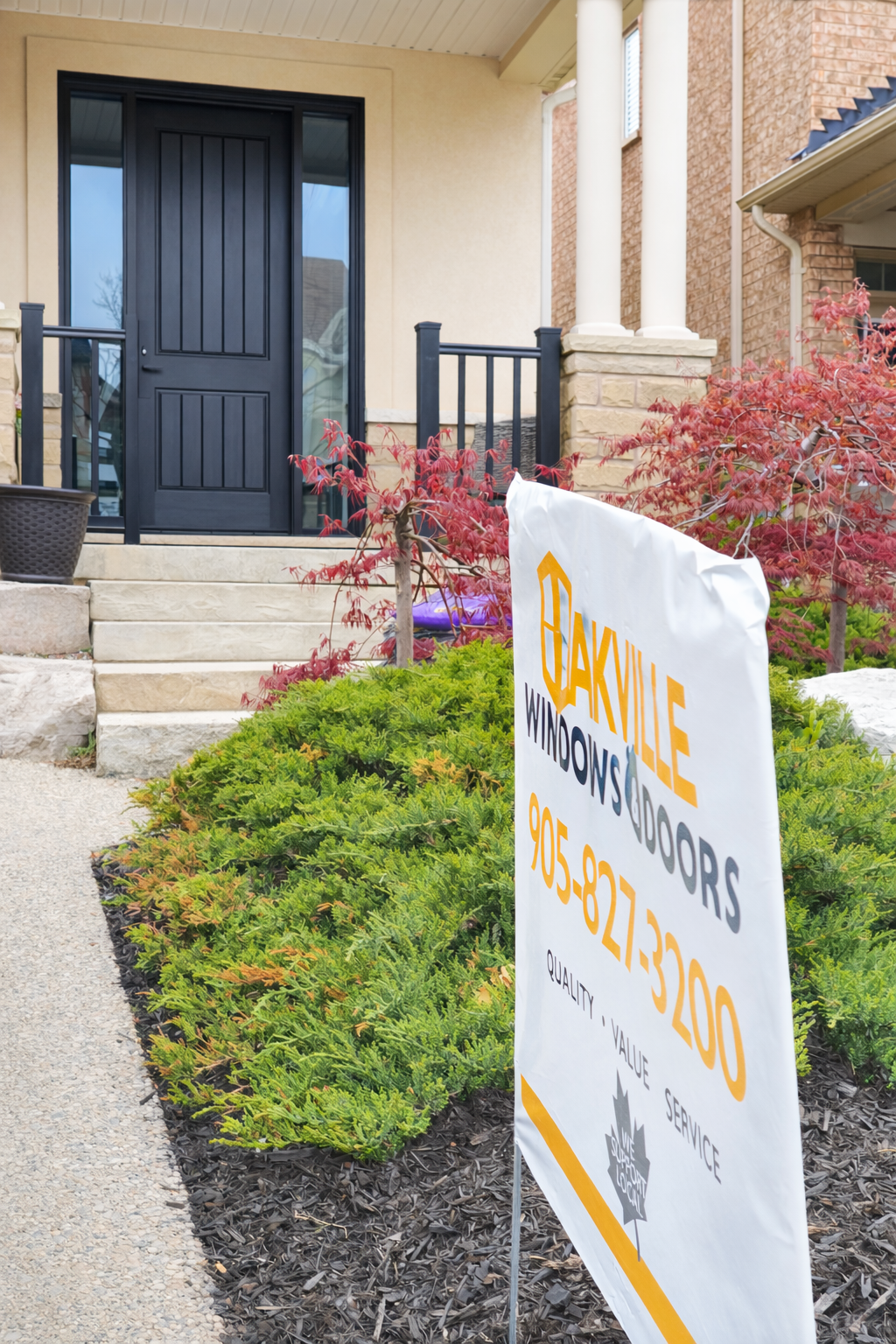 A business sign for Oakville Windows and Doors in front of a house entrance with a black door and stone steps.