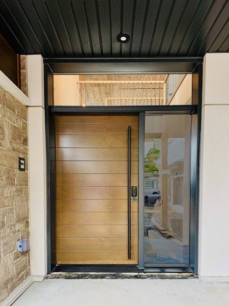 A modern front entryway with a horizontal wood-slat door, a vertical black handle, and a tall side glass panel.